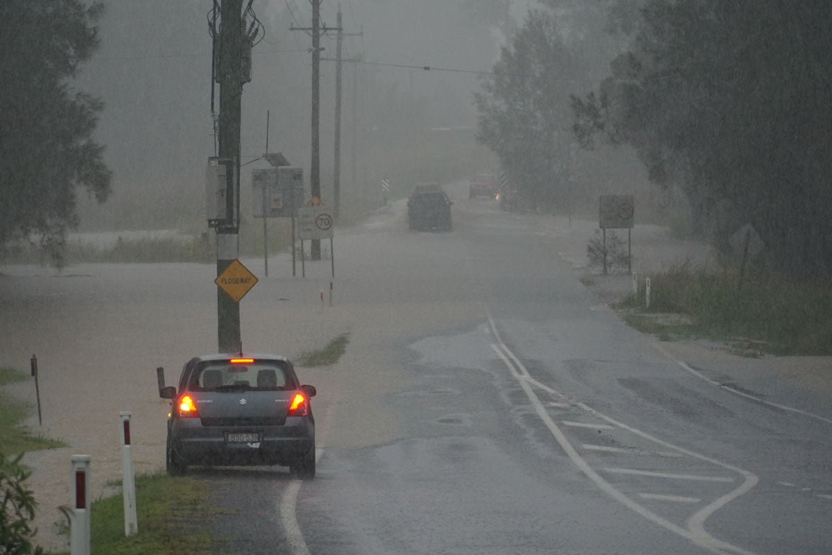 A grey car is pulled over to the side of a flooded road. It's pouring rain.         