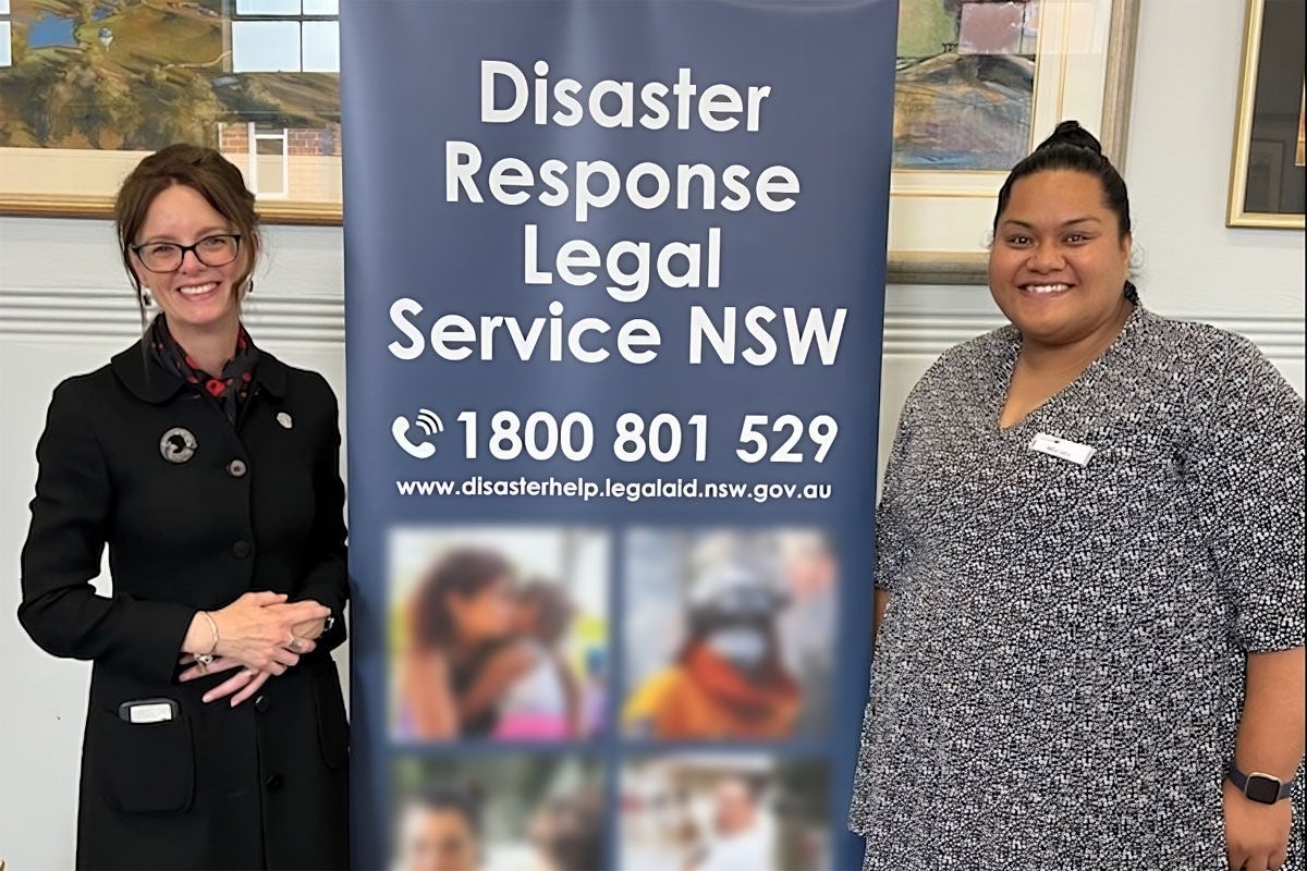 Steph Cooke and Ma'ata Solofoni stand either side of a Disaster Response Legal Service banner. They are smiling.