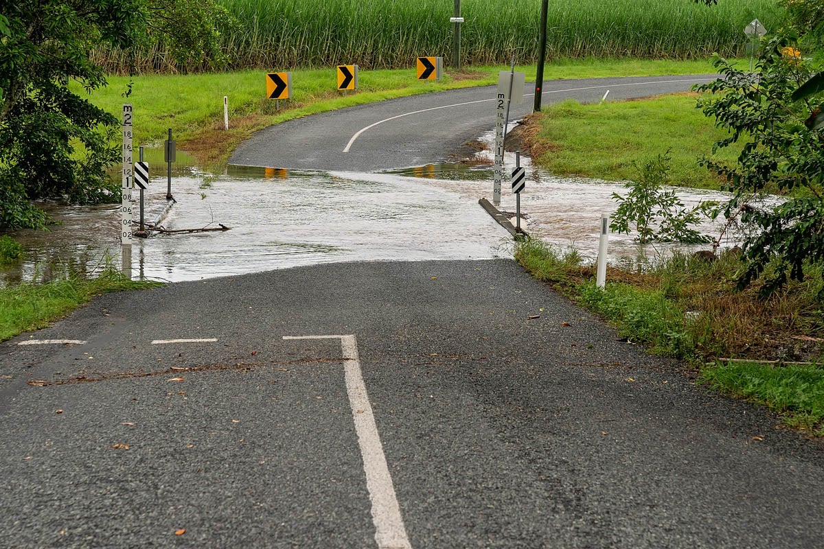 Water over the road from an overflowing creek caused by heavy tropical rainfall. Sign indicates depth.