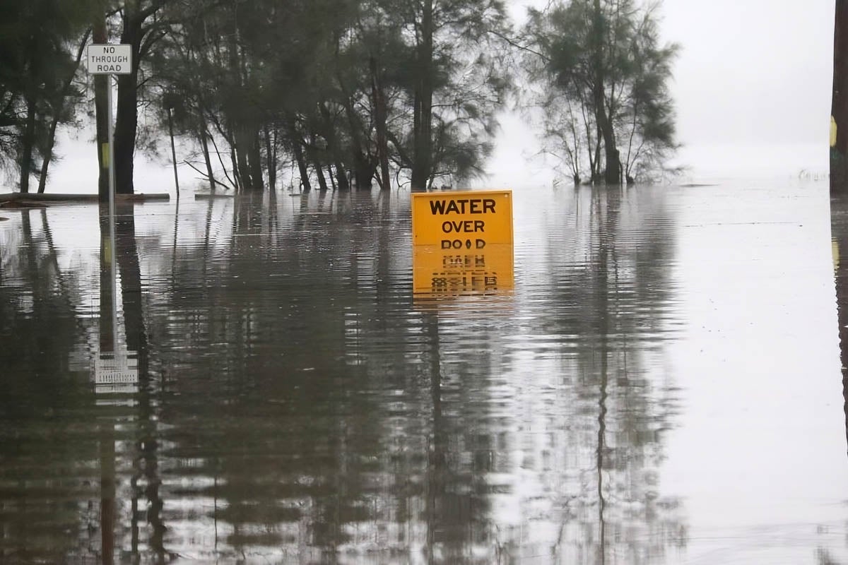 A yellow 'water over road sign' is just visible over the top of a flooded waterway. 