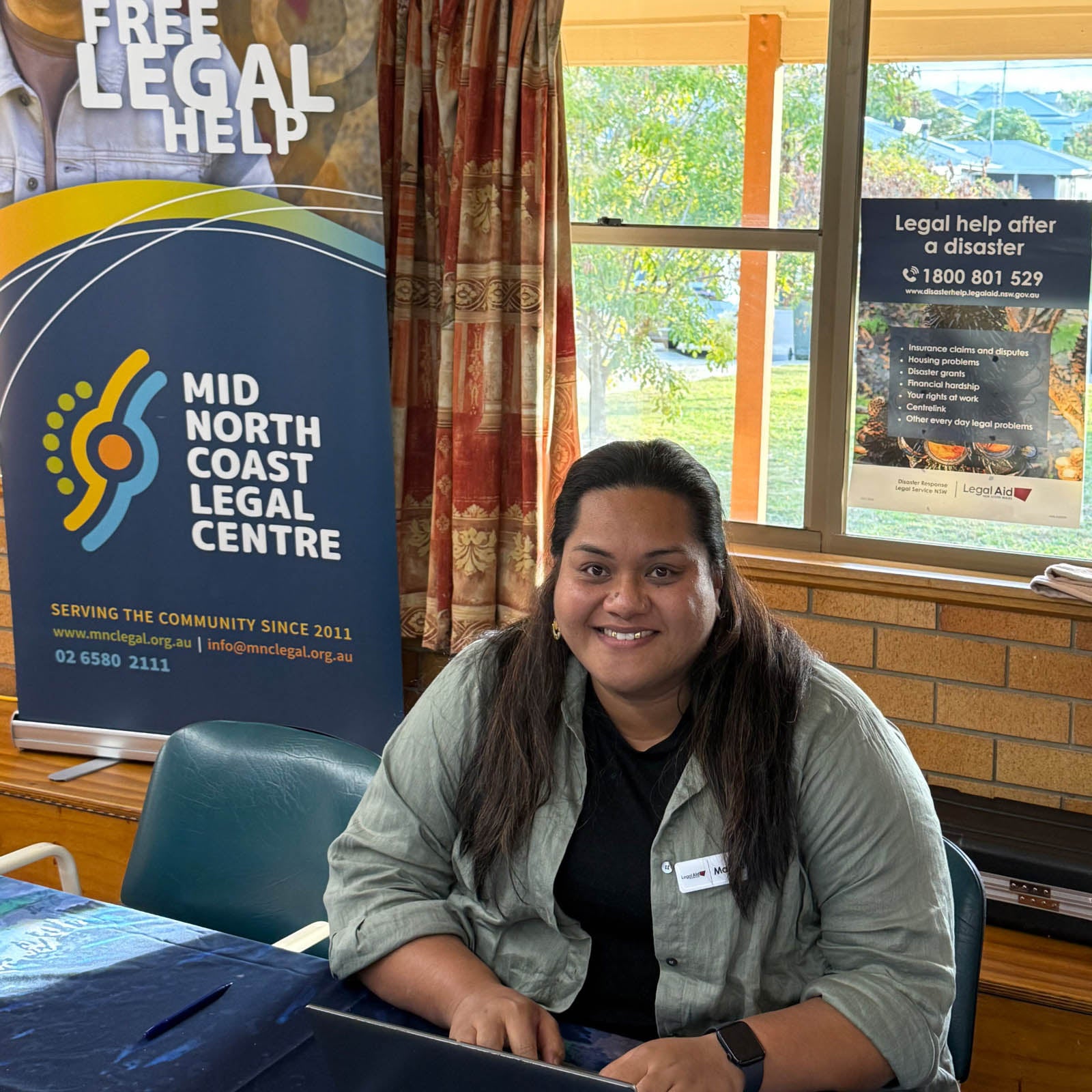 Senior solicitor Ma’ata Solofoni sitting at a table with a laptop at the Macksville Recovery Centre. There is a 'Mid North Coast Legal Centre' banner behind her.